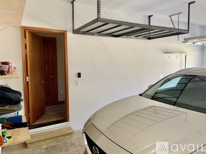 A car is parked in a garage with a wooden door and a metal shelf above it.
