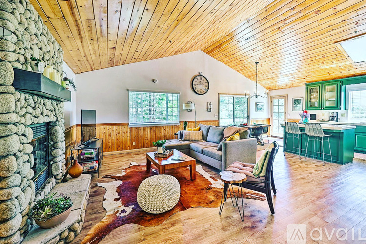 A living room with a stone fireplace and wooden ceiling.