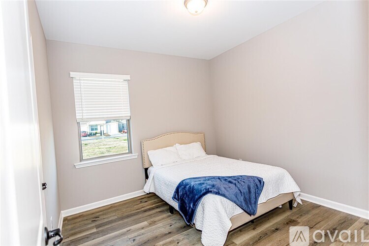 A bedroom with a bed, blue blanket, and a window with blinds.