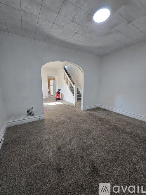 A room with a carpeted floor and a staircase leading to another room.