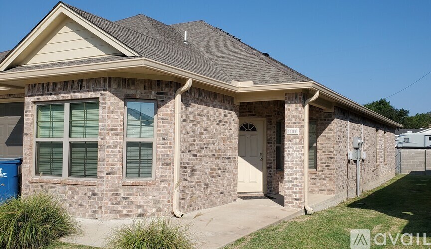A house with a blue trash bin in front of it.