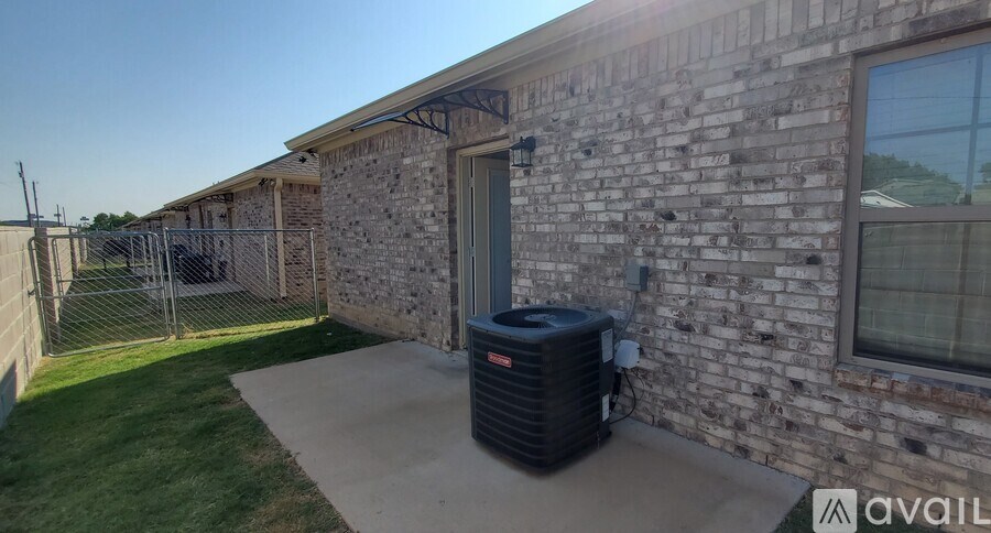 A black air conditioning unit sits on a concrete slab outside a brick building.