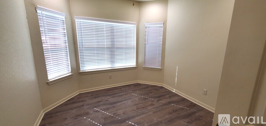 A room with wooden flooring and three windows with blinds.