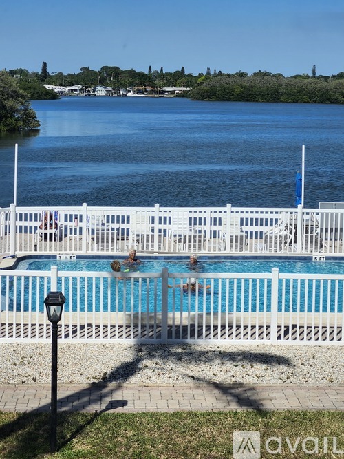 A white fence surrounds a blue pool with people swimming in it.