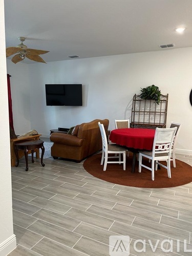 A living room with a brown sofa, a red tablecloth, and a television mounted on the wall.