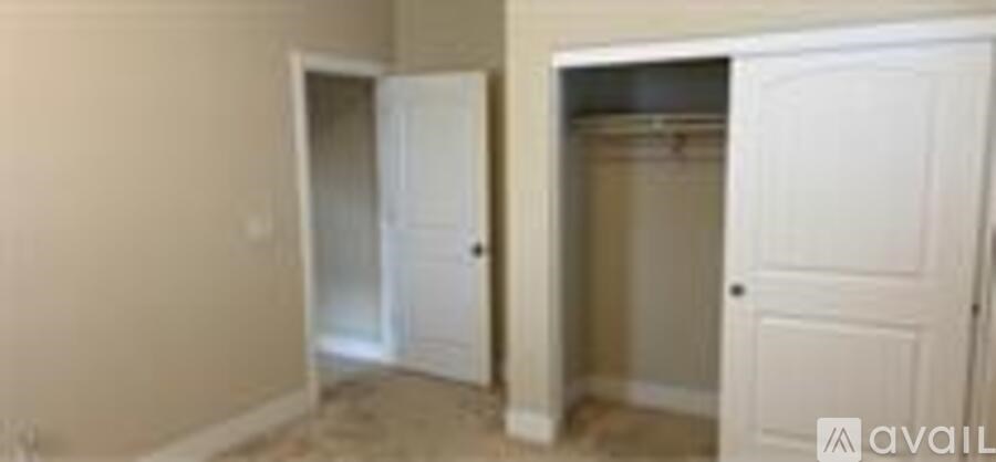 A room with a white door and a white closet with clothes hanging.