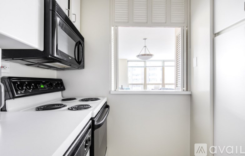 A kitchen with a white stove top oven and microwave, a window with blinds, and a hanging light fixture.