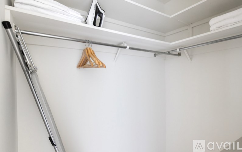 A white wall with clothes hangers and a clothes ironing board.