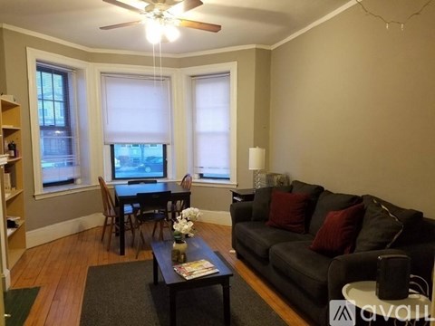 A living room with a black couch, a dining table with chairs, and a ceiling fan.