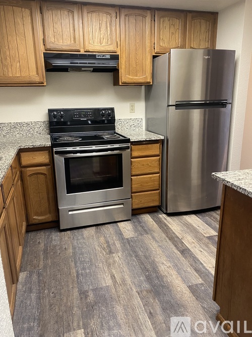 A kitchen with a stove top oven, a refrigerator, and wooden cabinets.