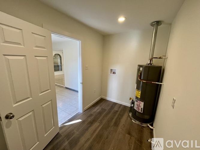 A room with a white door, a white wall, and a black water heater.