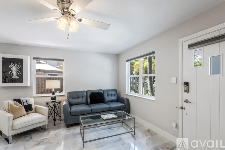 A living room with a grey couch, a white armchair, a glass coffee table, and a ceiling fan.