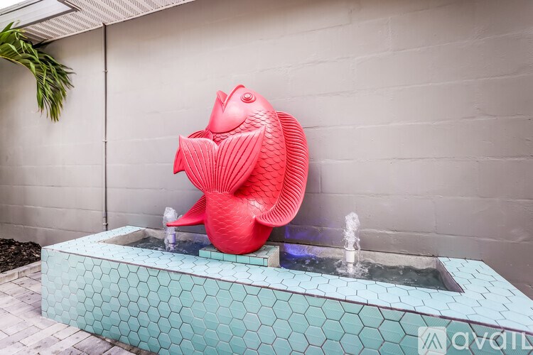 A red fish sculpture is sitting on a blue hexagonal tile fountain.