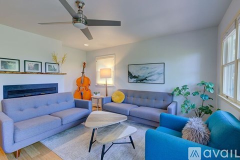 A living room with a grey couch, a blue chair, a white coffee table, a ceiling fan, and a guitar on the wall.
