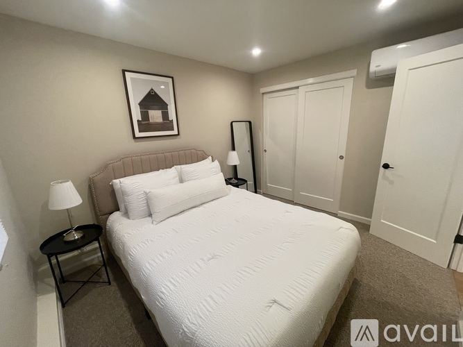 A bedroom with a large bed, a nightstand with a lamp, and a framed picture on the wall.