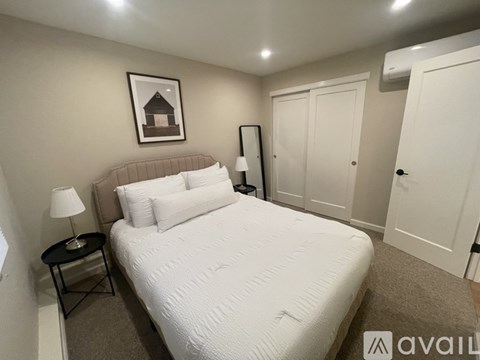 A bedroom with a large bed, a nightstand with a lamp, and a framed picture on the wall.