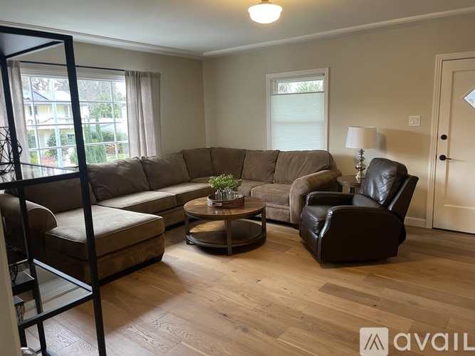 A living room with a brown couch, a black leather chair, and a wooden floor.