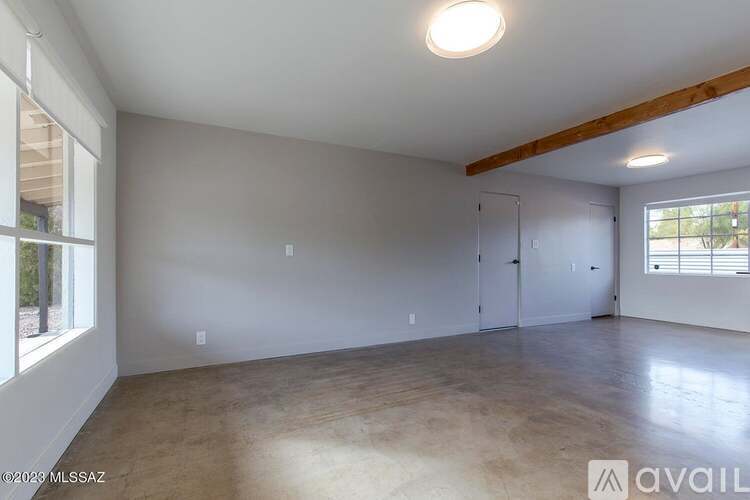 A spacious room with a wooden beam ceiling and a large window on the right side.
