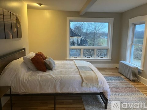 A bedroom with a large bed and a view of a fence and trees through the window.