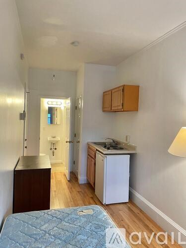 A bedroom with a bed, a dresser, a fridge, and a cabinet.