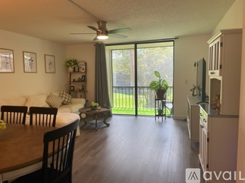 A living room with a dining table and chairs, a ceiling fan, and a view of a backyard through a sliding glass door.