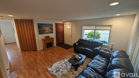 A living room with a black leather couch and a wooden floor.