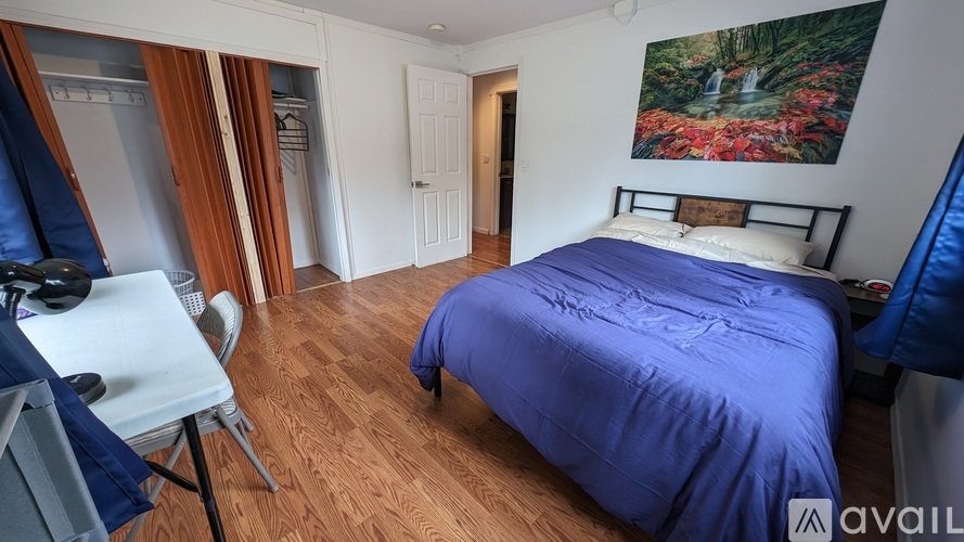 A bedroom with a blue bedspread and a painting on the wall.