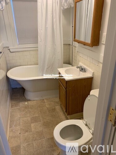 A white toilet is in a bathroom with a white tub and sink.