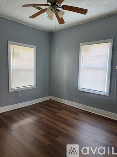 A room with a ceiling fan and two windows.