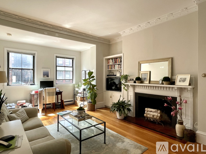 A living room with a fireplace, a couch, a chair, a coffee table, a potted plant, a bookshelf, and a mirror.