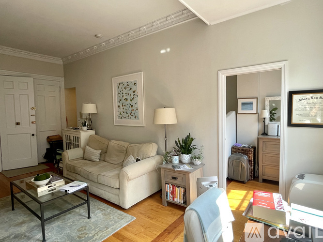 A living room with a white couch, a glass coffee table, and a lamp on a side table.