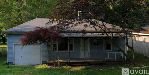 A small house with a porch and a tree in front.