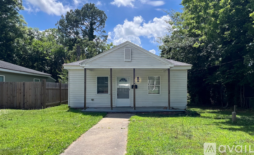 A small white house with a porch and a sun shining in the background.