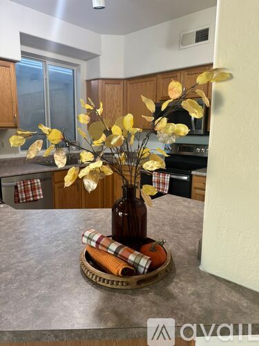 A brown bottle with yellow leaves in it sits on a wooden tray.