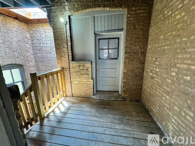 A wooden deck leads to a white door in a brick wall.