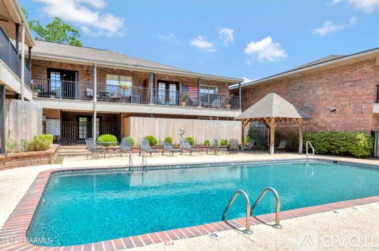A large outdoor swimming pool with a red brick wall and a wooden deck with chairs and a table.