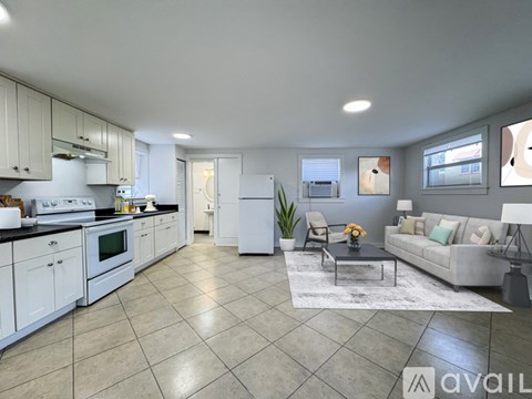 A modern kitchen with white cabinets and appliances, a dining table with chairs, and a living room with a couch and decorative pillows.
