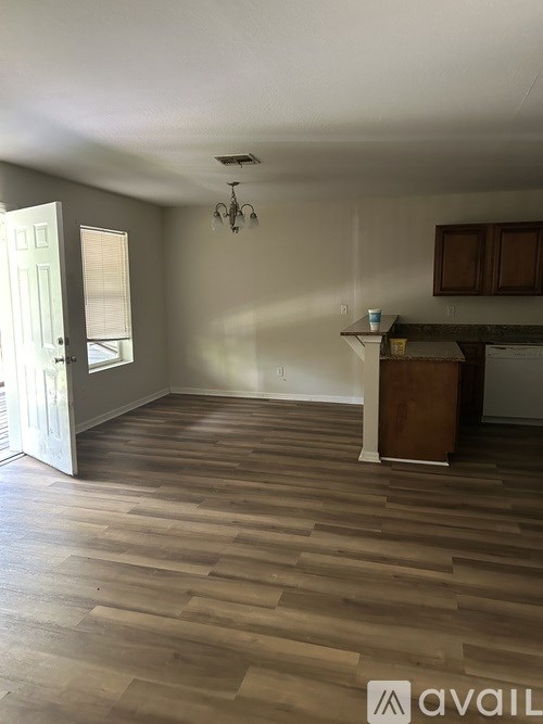 A room with wooden flooring and a kitchen area in the background.