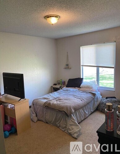 A bedroom with a bed, a television, and a window with blinds.