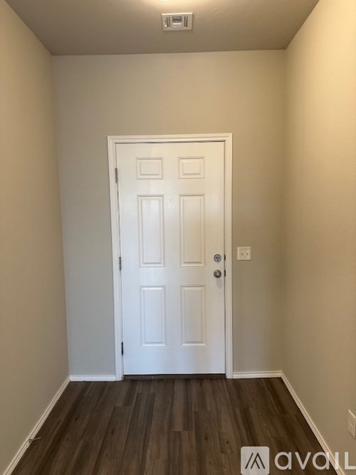 A white door is in the middle of a room with wood flooring.