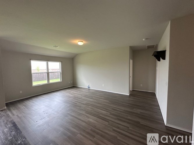 A spacious room with wooden flooring and a large window.