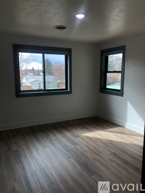 A room with wooden flooring and two windows.
