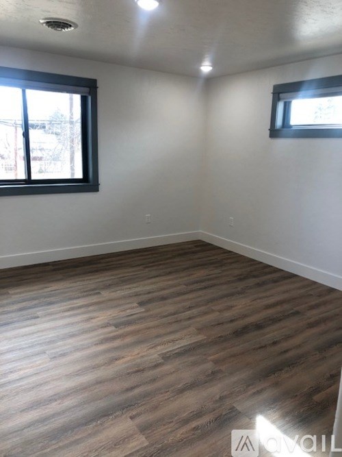 A room with wooden flooring and two windows.