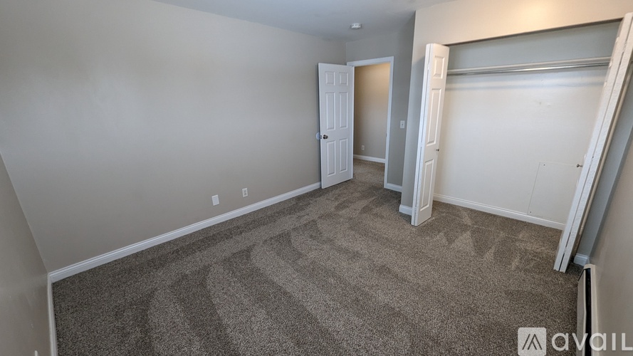 A carpeted room with a door and a wall with a window.