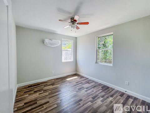 A room with a ceiling fan and two windows.