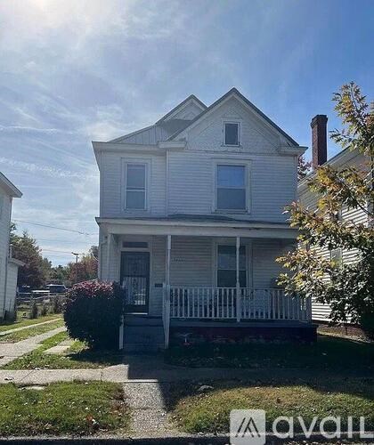 A two-story house with a front porch and a tree in front.