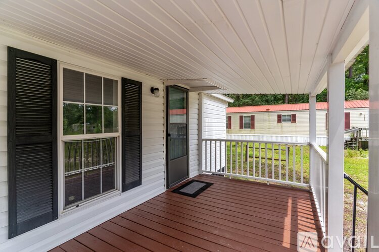 A white house with a brown deck and black shutters.