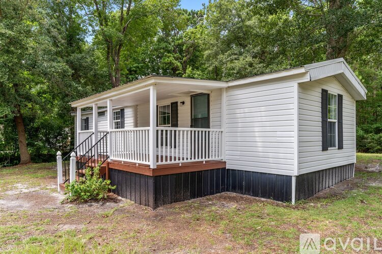 A small house with a porch is surrounded by trees.