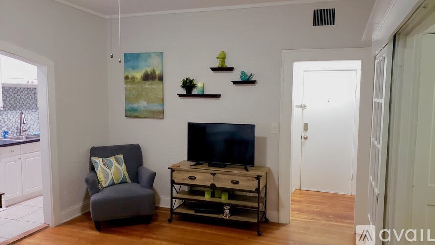 A living room with a grey armchair, a television, and a painting on the wall.