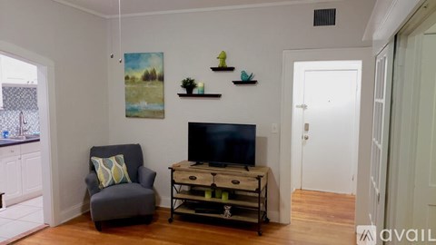 A living room with a grey armchair, a television, and a painting on the wall.